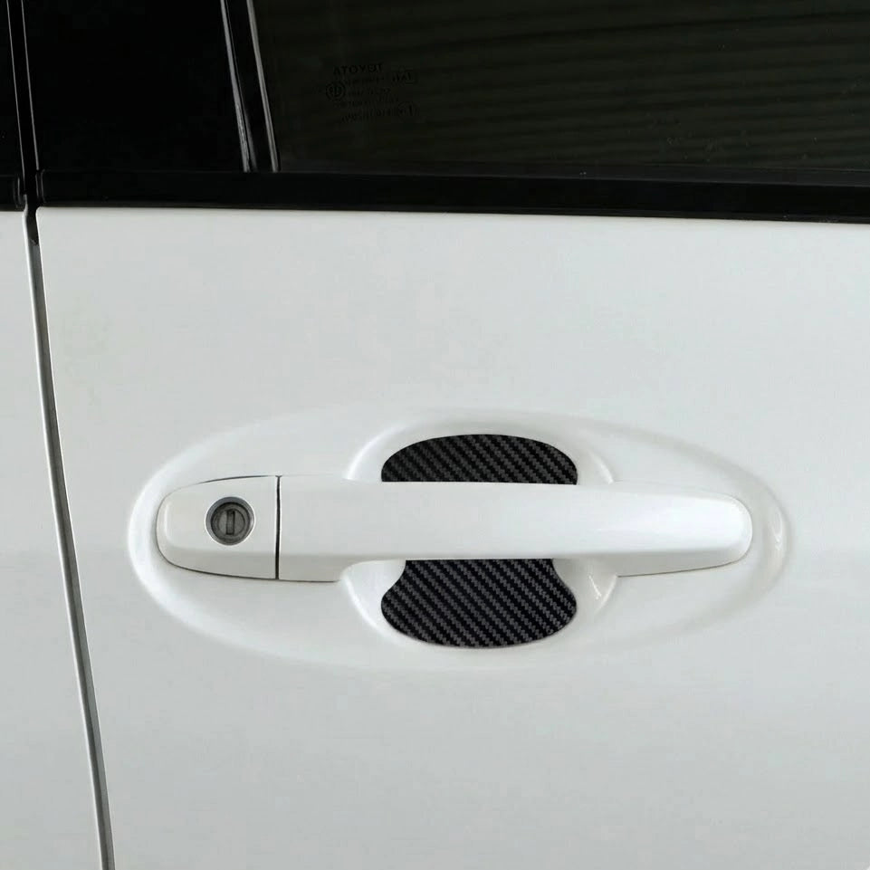 Black carbon fiber car door handle scratch protector installed behind door handle on white car exterior. A fun Car-Wah! car accessory statement piece that adds instant personality.