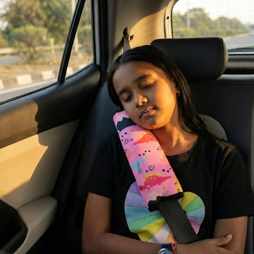 A young girl napping comfortably in a car seat using a pink Car-Wah! plush seatbelt cover with a dinosaur print.Making traffic a little more fun with Car-Wah! comfort car accessories.