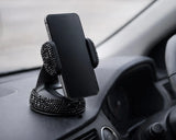 Black bling car phone holder mounted on dashboard holding smartphone. view of a phone mounted in the rhinestone holder during a daily drive, a quirky Car-Wah! accessory that adds instant personality.
